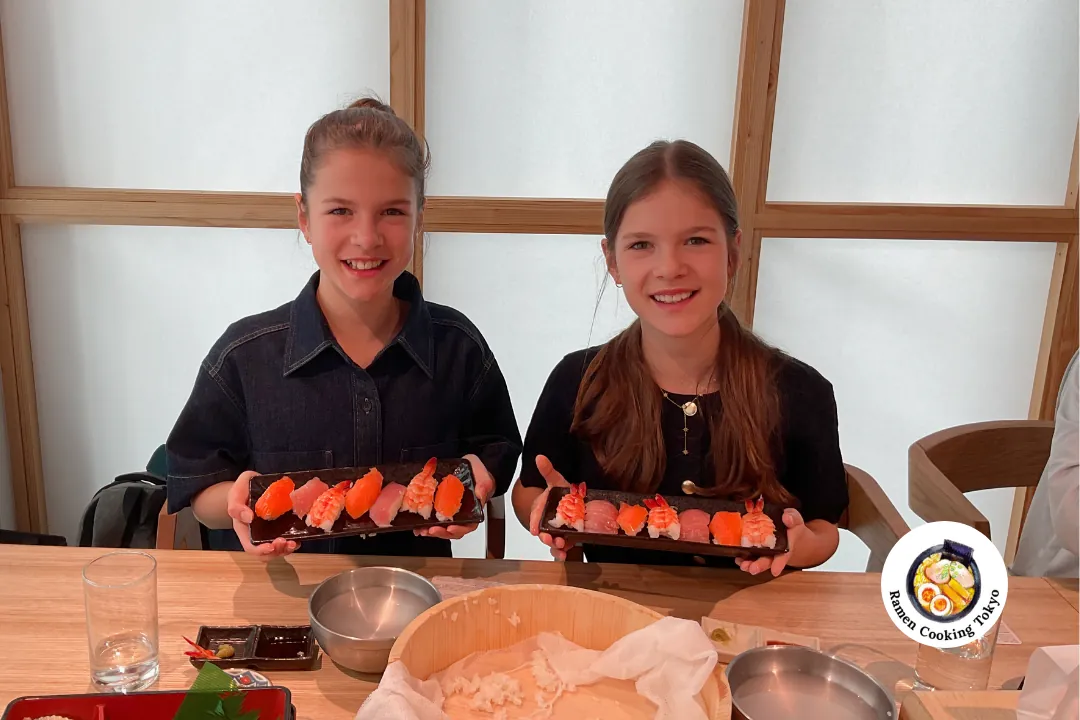 Due bambine mostrano con orgoglio i loro sushi fatti a mano in un corso di cucina per bambini a Tokyo