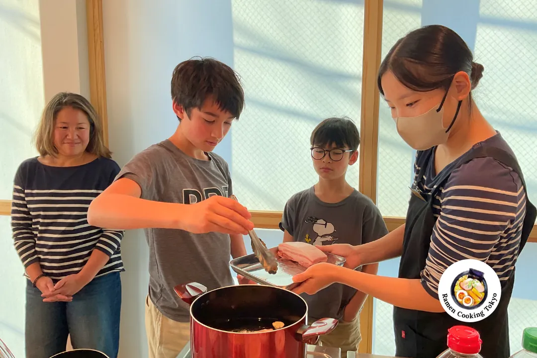 Un adolescente prepara il brodo di ramen con la guida dell&rsquo;istruttrice in un corso di cucina per famiglie a Tokyo